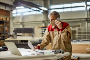 Un artisan plombier assis à son bureau le soir, ordinateur portable ouvert sur une liste de devis à traiter.